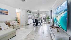 Un salon moderne doté d’un grand téléviseur à écran plat, d’un coin repas avec une table et des chaises, et d’un espace salon confortable avec des canapés.