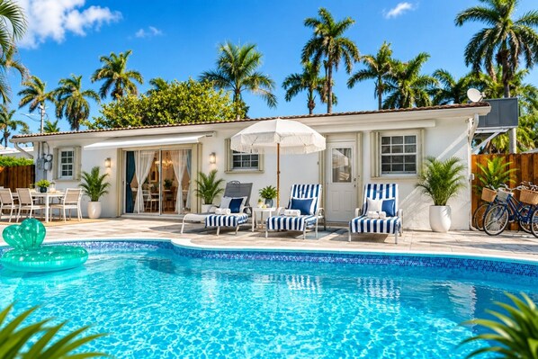 A poolside area with lounge chairs, a pool, and a building with a tiled roof.