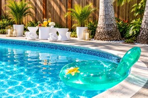 Une piscine dont le bord est orné d’une mosaïque bleu clair, entourée de meubles d’extérieur blancs et de plantes en pot.