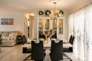 Un coin repas avec une table blanche, des chaises noires et un lustre. Derrière la table, on aperçoit un buffet blanc aux portes vitrées.