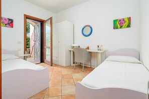 A bedroom with two beds, a desk, a chair, a wardrobe, and a bathroom visible through an open door.