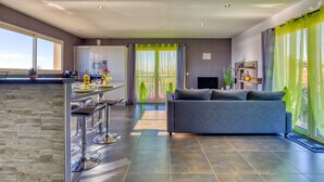 A modern kitchen with a bar area, a grey sofa, and a large sliding glass door to the outdoors.