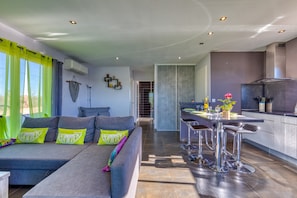 A modern living area with a sofa, bar stools, and a kitchen area.
