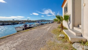 A coastal building with a gravel path leading to a marina with boats.