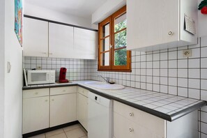 Une cuisine compacte avec des meubles blancs, un four à micro-ondes, une machine à café rouge et une fenêtre donnant sur un paysage verdoyant.