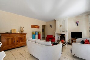 Ein Wohnzimmer mit einem Holzkabinett, weißen Sofas, einem roten Sessel, einem Kamin und einem Fernseher.