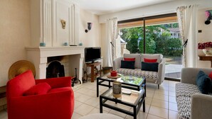 A living room with a fireplace, television, and seating area with a view to the outdoors. - Holiday Home 'Villa Entre Océan Et Pinède' with Private Terrace, Private Garden and Wi-Fi (La Tremblade)