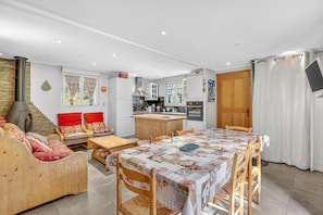 A modern kitchen with a central island, wooden furniture, and a dining area with a table set for four. - Chalet "Ma Bonne Etoile" with Mountain View, Private Terrace and Wi-Fi (Méolans-revel)