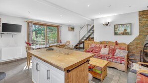 Een ruime woonkamer met een houten eettafel, een bank en een trap naar een verdieping erboven.