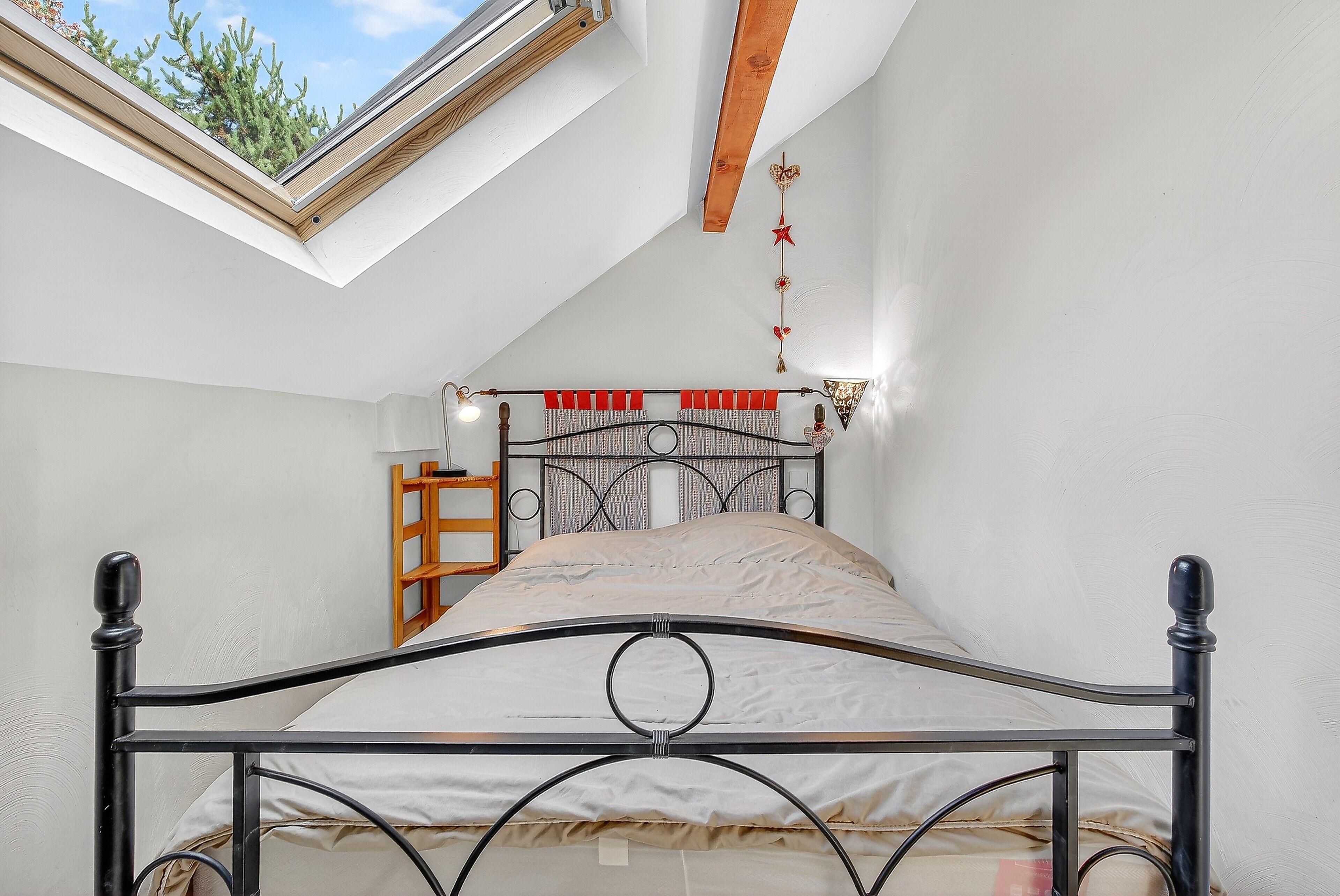 Una cama individual con estructura metálica, un tragaluz arriba y una viga de madera.