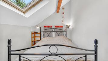 Una cama individual con estructura metálica, un tragaluz arriba y una viga de madera.