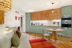 A modern kitchen with wooden cabinets, a dining area with a round table and chairs, and a built-in oven. - Casa de São Pedro Sintra – Cozy House with Wi-Fi (Sintra)