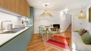 Une cuisine moderne avec un coin repas, des meubles en bois, un plan de travail blanc et un tapis coloré.