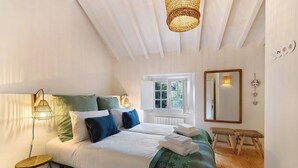 Une chambre à coucher avec un lit, des lampes de chevet, une fenêtre, un miroir et un banc.