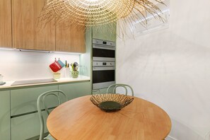 A kitchen with a round wooden table, a wire basket, and a hanging light fixture. - Casa de São Pedro Sintra – Cozy House with Wi-Fi (Sintra)
