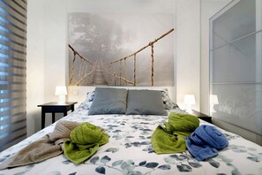 Cama bem arrumada com colcha florida, duas almofadas e uma obra de arte de ponte de corda na parede.