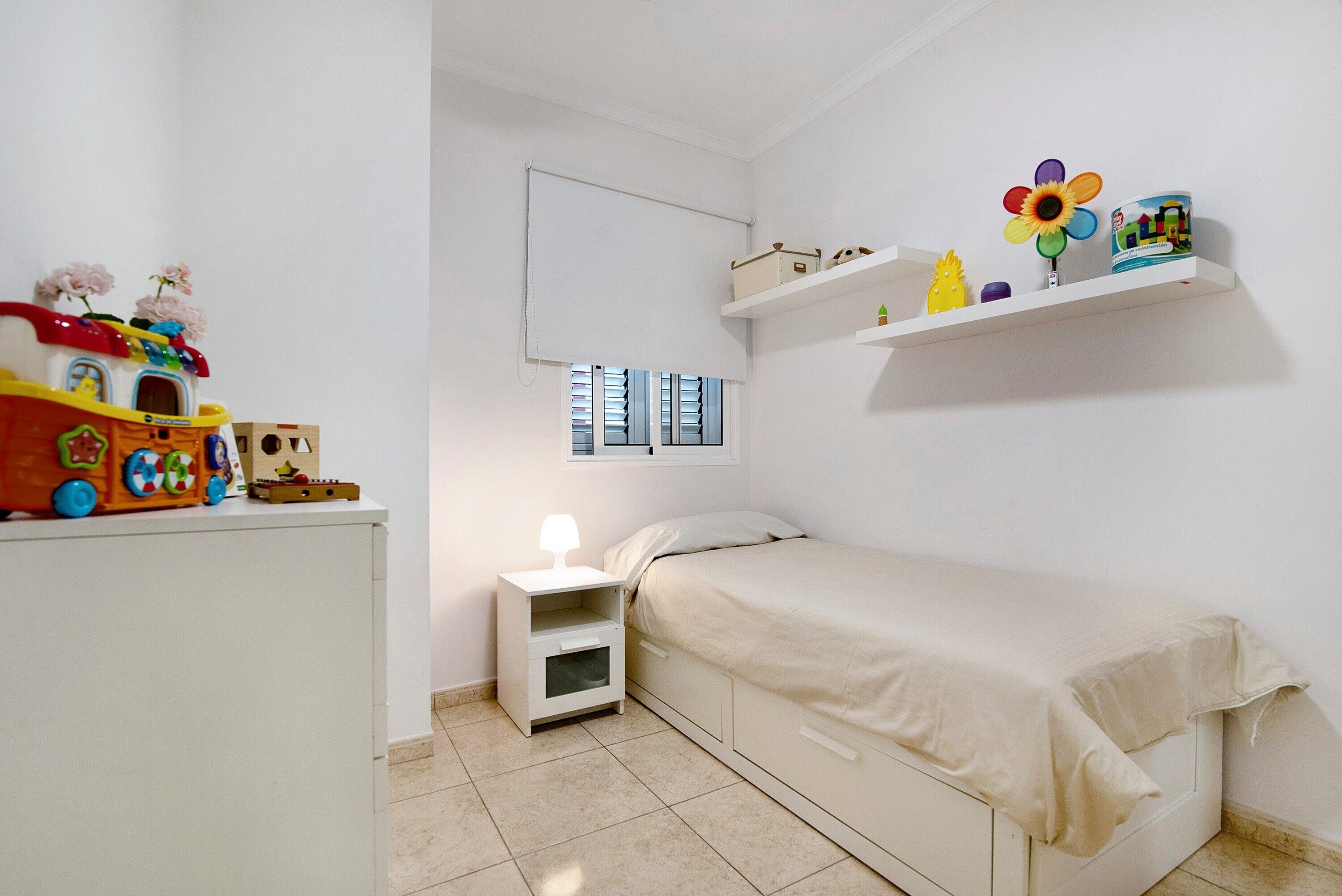 A child's bedroom with a bed, nightstand, and a toy train on a dresser.