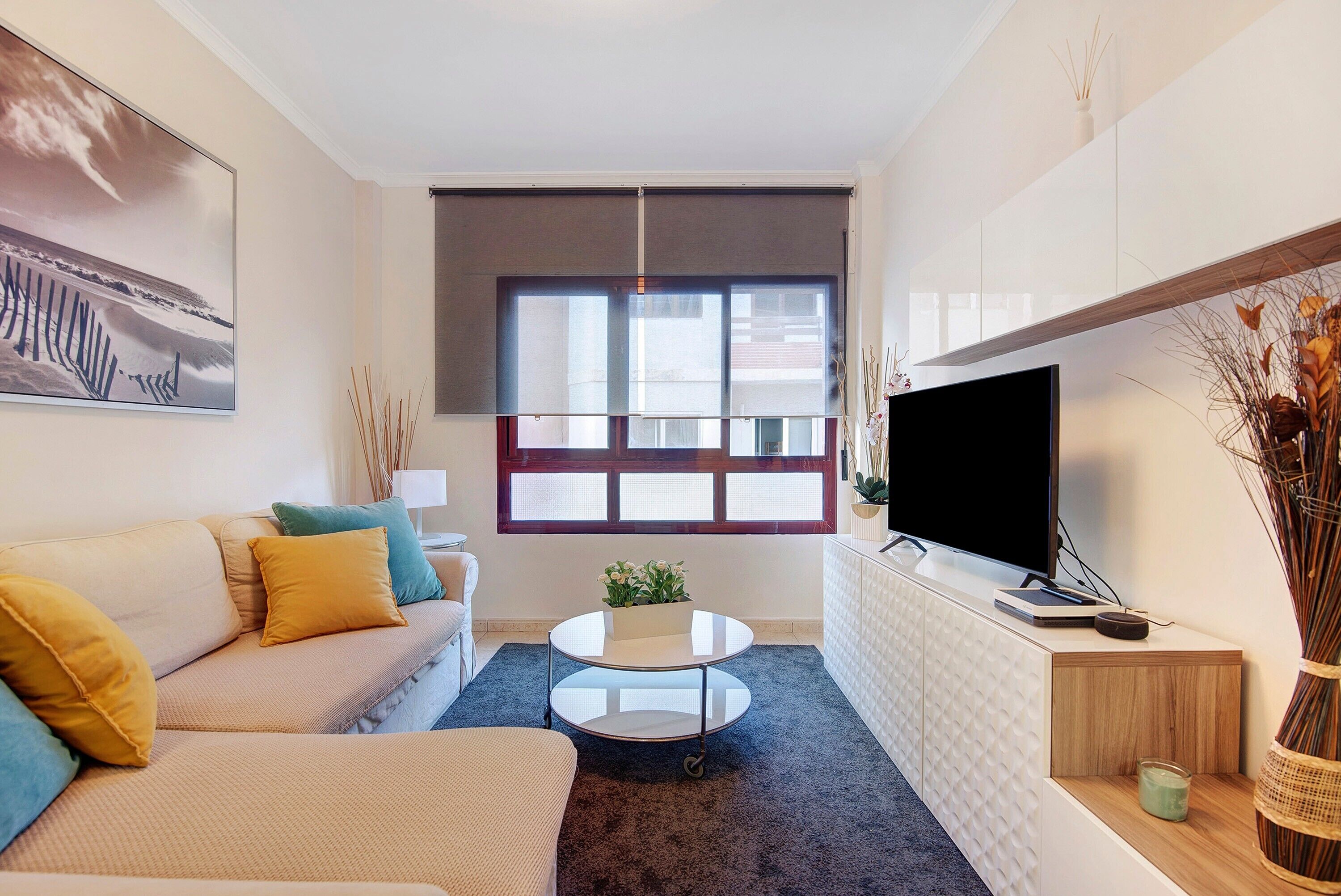 A modern living room with a sofa, coffee table, TV, and a large window.