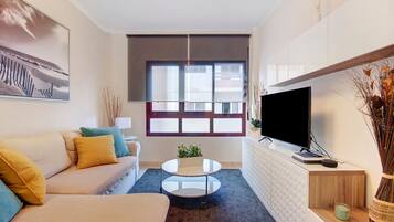A modern living room with a sofa, coffee table, TV, and a large window.