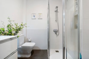 A modern bathroom with a toilet, shower, and two framed pictures on the wall. - Vacation Home "Apartamento Playa de Las Canteras" with Wi-Fi (Las Palmas de Gran Canaria)