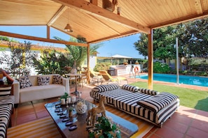 A covered outdoor seating area with a pool, a sofa, a table, and a dining set.