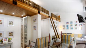 Una sala de estar con una mesa de centro de vidrio, sofás a rayas, una escalera de madera y una estantería.
