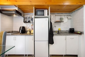 A compact kitchen with white cabinets, a microwave, a coffee maker, and a hanging pot rack.