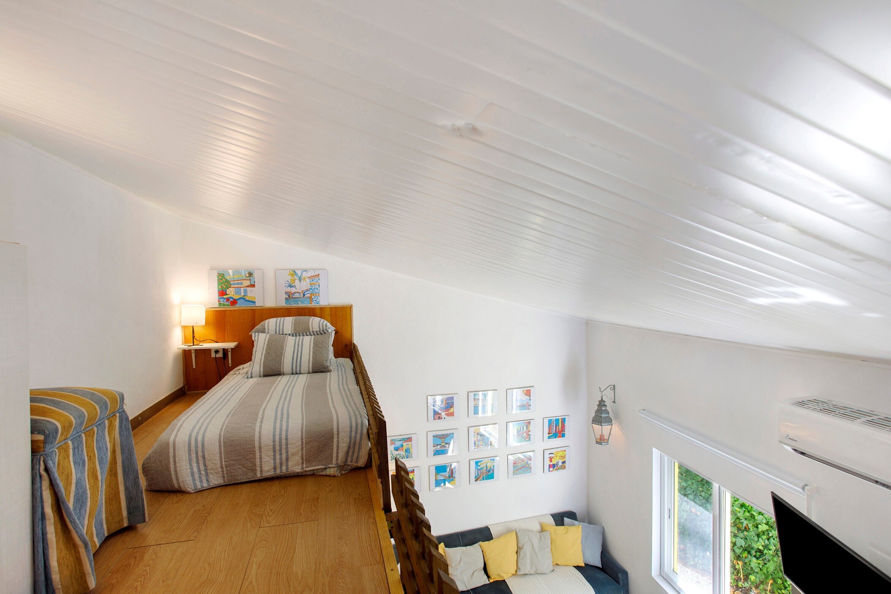 Une chambre à coucher comprenant un lit, une table de chevet, une lampe, un climatiseur fixé au mur et une fenêtre donnant sur un paysage verdoyant.
