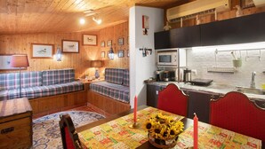 A cozy cabin interior with a wooden ceiling, a dining area with a table set for two, a kitchen with a microwave, and a seating area with a sofa.