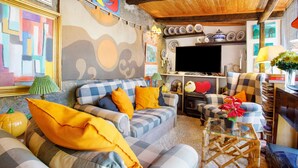 A cozy living room with checkered sofas, a flat-screen TV, and a rustic wooden ceiling.