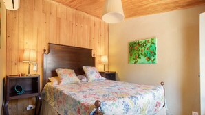 A wooden-paneled bedroom with a bed, two bedside lamps, a nightstand, and a painting on the wall.
