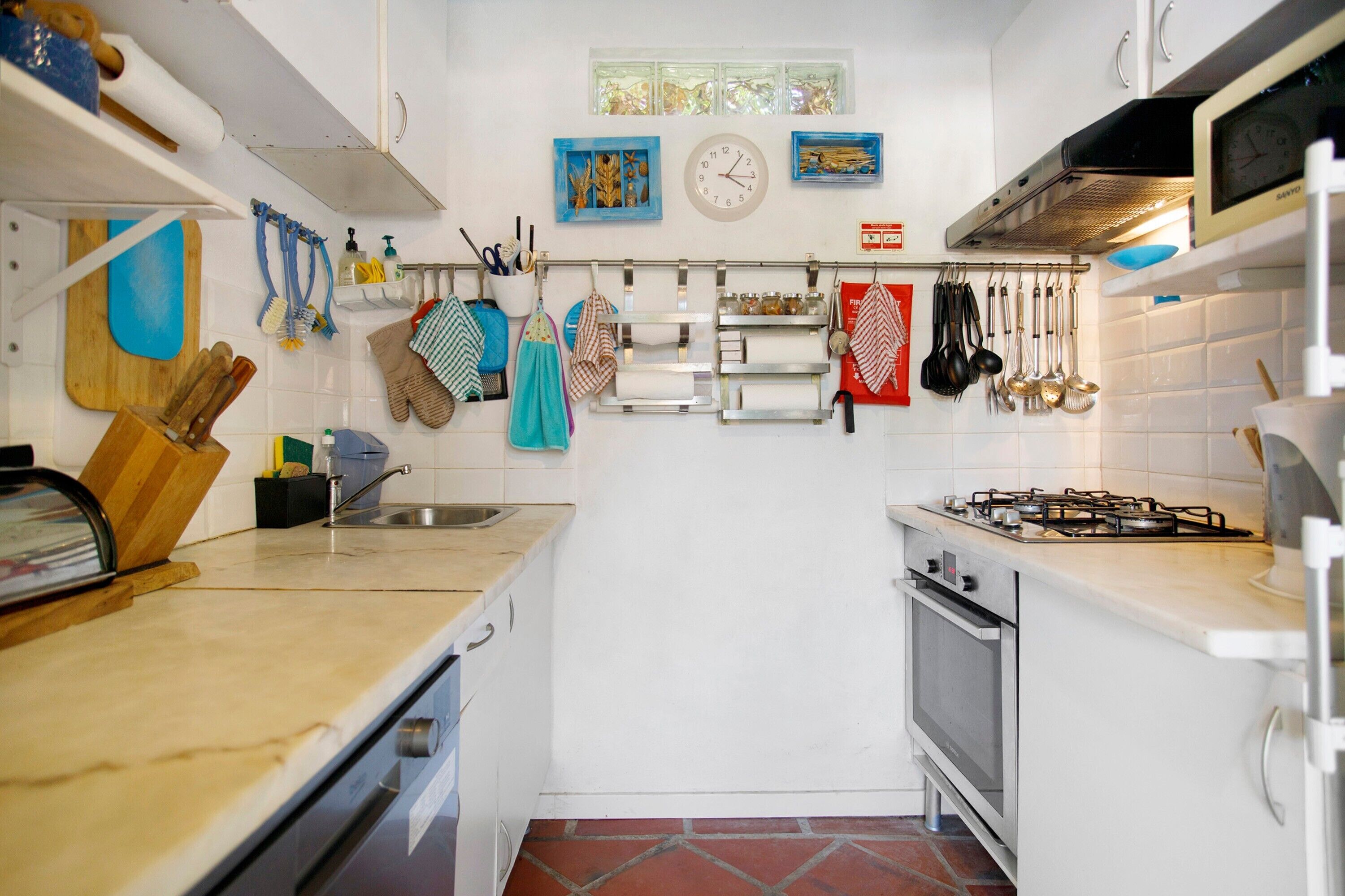 Een keuken met witte kastjes, een gasfornuis, een spoelbak en diverse keukengerei aan de wand.