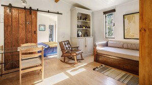 Una sala de estar acogedora con un sillón mecedor de madera, una mesa de vidrio, un sofá y un aparador con objetos decorativos.
