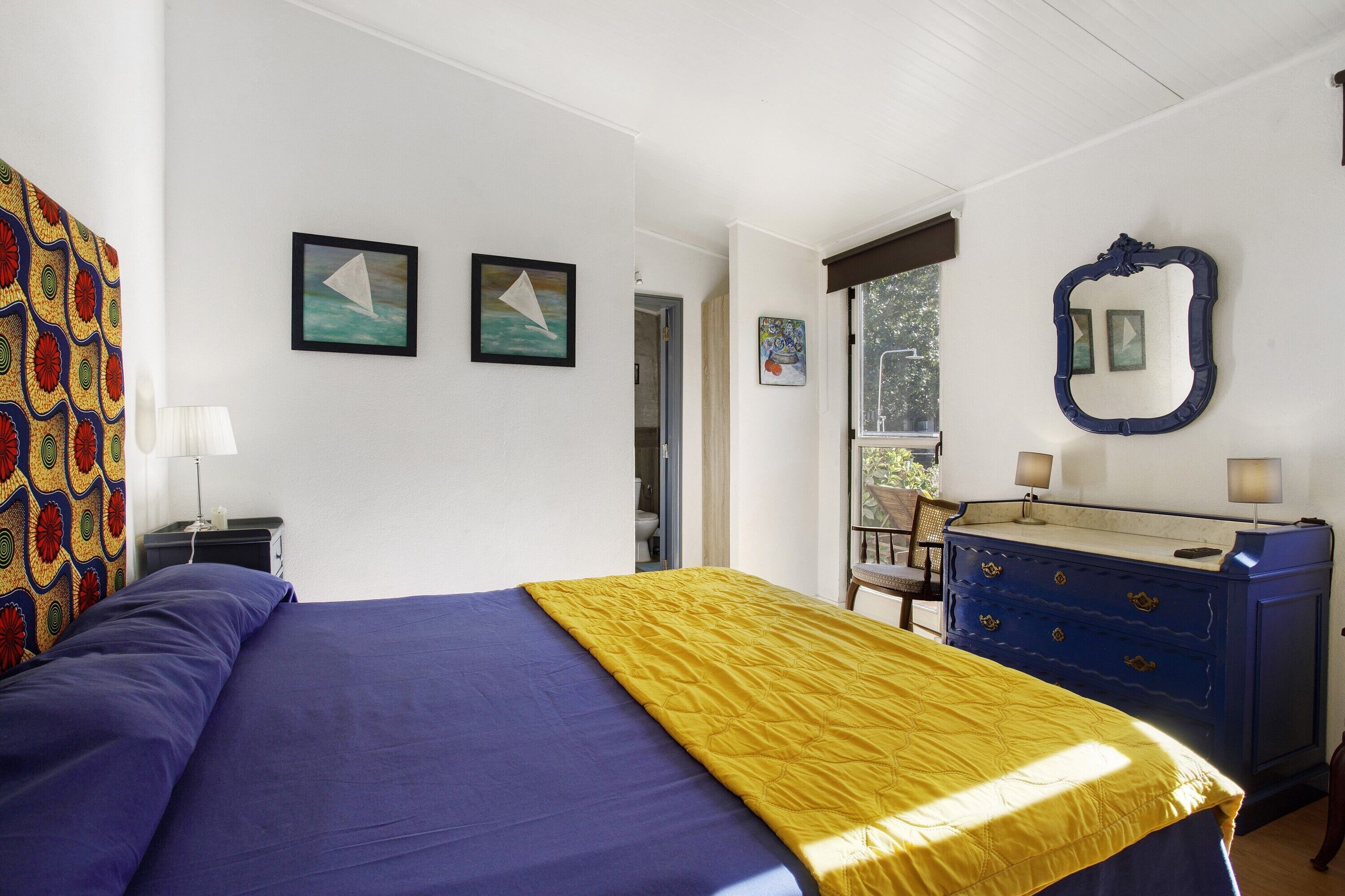 A bedroom with a bed, a dresser, a mirror, and artwork on the walls.