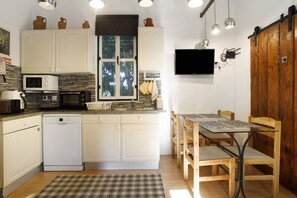 Une cuisine compacte avec des meubles blancs, un lave-vaisselle, un four à micro-ondes, une cuisinière et une table à manger avec des chaises.