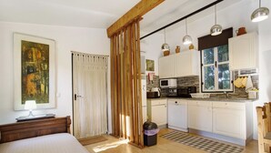 Un dormitorio con cama, mesita de noche, ventana con cortinas y un cuadro en la pared.