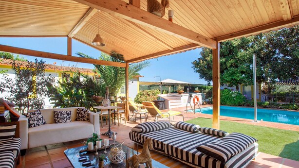 Un área de estar al aire libre techada con piscina, un sofá, una mesa y un conjunto de comedor.