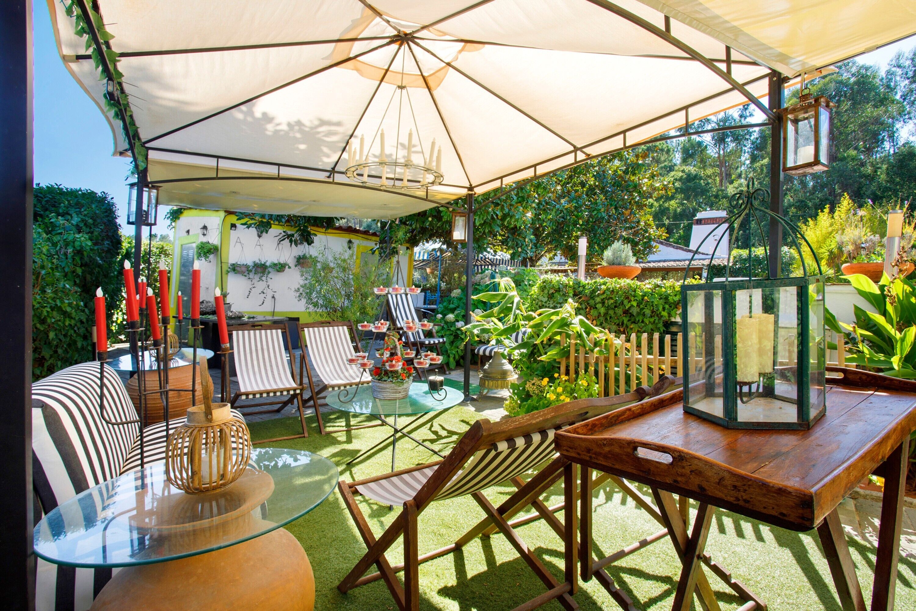 Une terrasse extérieure avec une table en verre, des chaises à rayures, une table en bois et une lanterne suspendue.