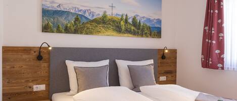 Habitación de hotel con cama, mesita de noche, lámpara de pared y un cuadro de un paisaje montañoso.