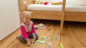 Un bambino seduto sul pavimento in una stanza con un letto a castello, pavimento in legno e una parete bianca.