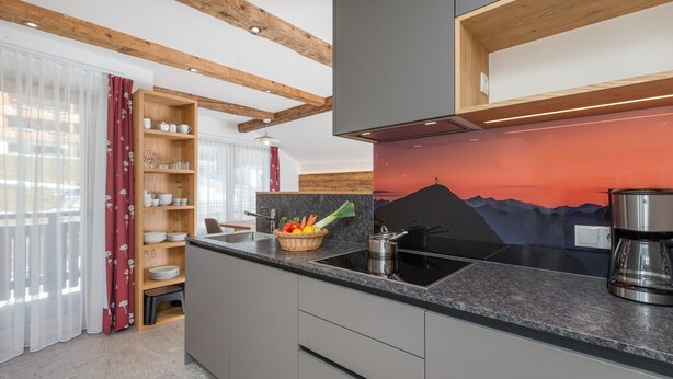 Una cucina moderna con travi in legno, un piano di lavoro nero e un murale con vista sulle montagne.
