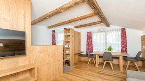 Un interno in legno con una TV, scaffali di legno, un tavolo da pranzo con sedie e una finestra con tende.