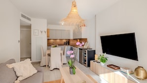 A modern living room with a sofa, a coffee table, a TV, and a kitchen in the background. - Apartment 'Le Jasmin' with Private Terrace, Wi-Fi and Air Conditioning (Nice)