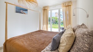 A bedroom with a bed, a hanging light fixture, a window with curtains, and a view of greenery outside. - Apartment 'Le Jasmin' with Private Terrace, Wi-Fi and Air Conditioning (Nice)