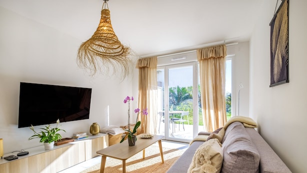 A modern living room with a flat-screen TV, a sofa, a coffee table, and a large window with curtains. - Apartment 'Le Jasmin' with Private Terrace, Wi-Fi and Air Conditioning (Nice)