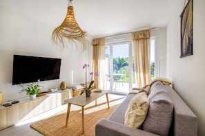 A modern living room with a flat-screen TV, a sofa, a coffee table, and a large window with curtains.