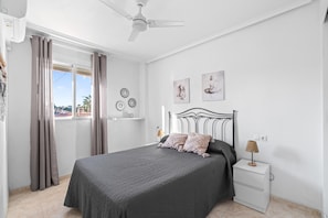 A bedroom with a bed, a nightstand, a ceiling fan, and a window with curtains.