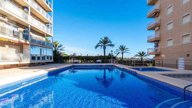 A swimming pool with clear blue water, surrounded by balconies and palm trees.