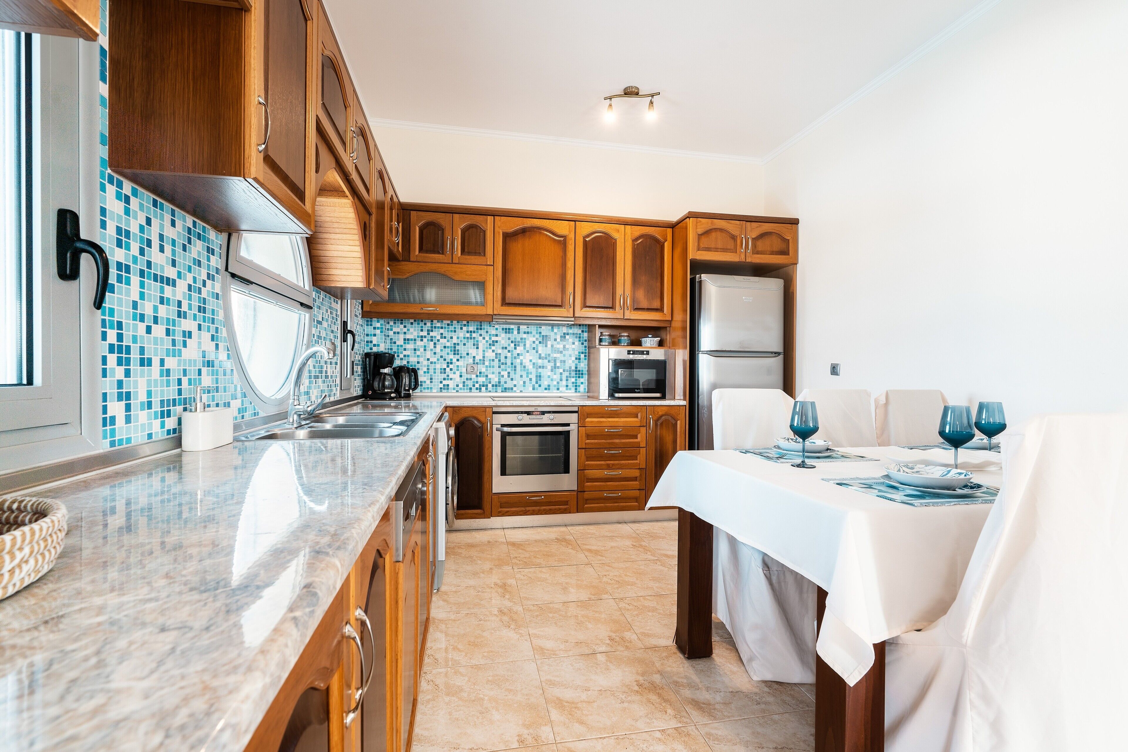 Una cocina con armarios de madera, salpicadero de azulejos, refrigerador de acero inoxidable y una mesa de comedor lista para cuatro comensales.