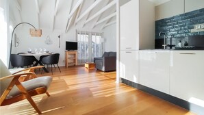 Cozinha moderna com armários brancos e painel de fundo preto, área de jantar com mesa e cadeiras, e uma janela grande com persianas.